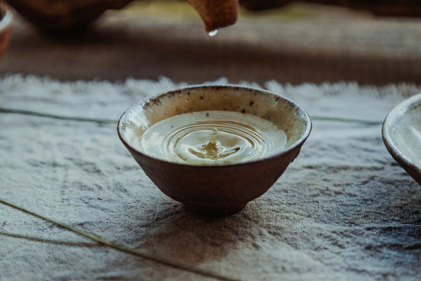 Ein Matcha Pot mit einem Matcha Besen und einer Matcha Schüssel mit Matcha Pulver auf dem Tisch neben einem Leinentuch